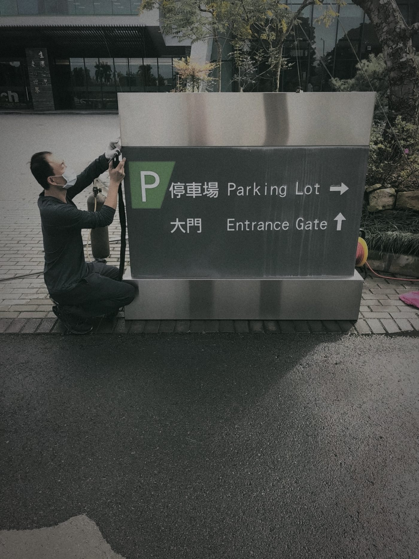 師傅蹲在不鏽鋼停車場指示牌旁維修